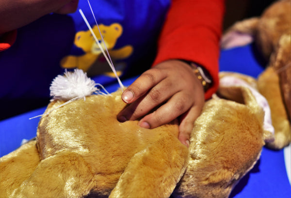 Someone stitching up a teddy bear stuffed animal